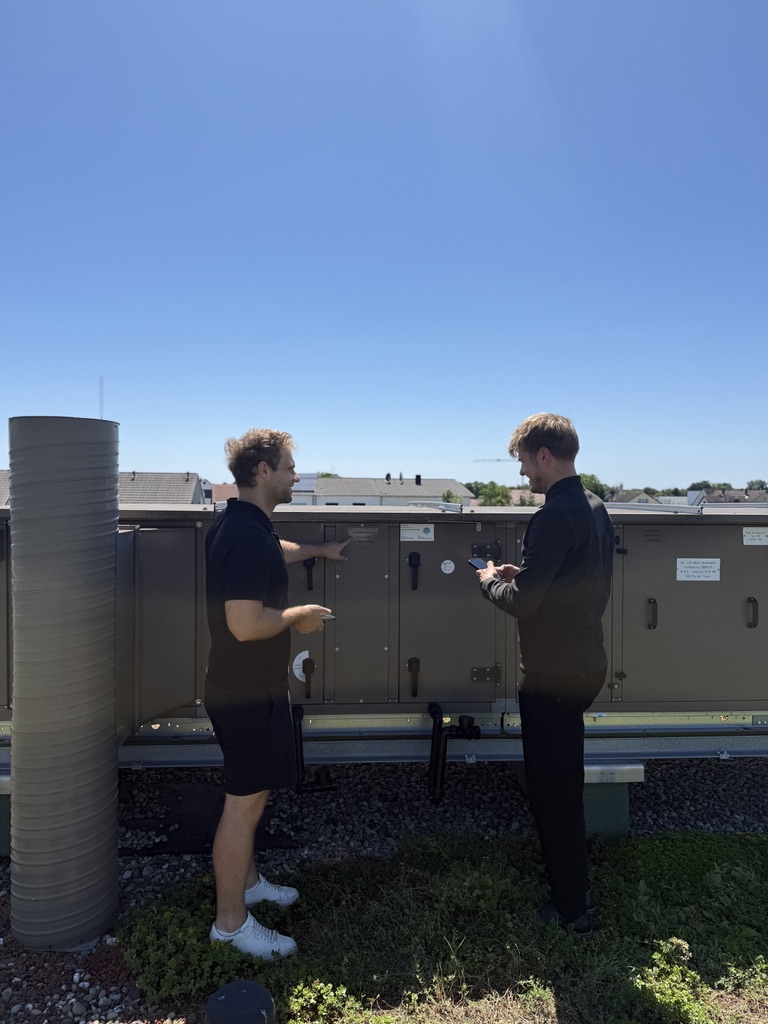 Lucas Pfeiffer und Bernhard Schochenmaier bei der Begehung auf einem Flachdach, vor einer Lüftungsanlage