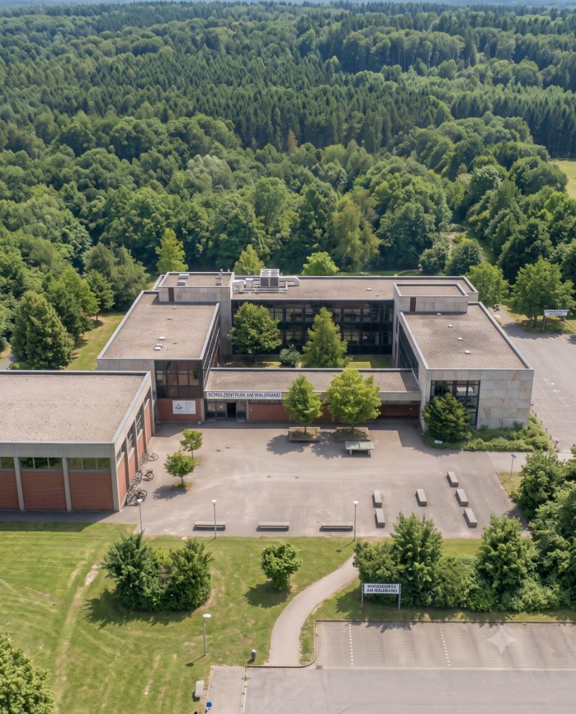 Luftaufnahme eines Schulzentrums mit Flachdächern am Waldrand